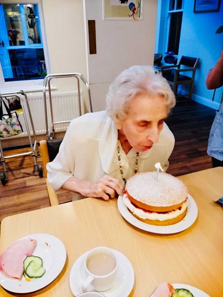 Elderly lady blowing out a candle on a cake.