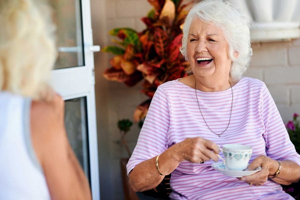 Happy elderly lady drinking tea and laughing with friends.